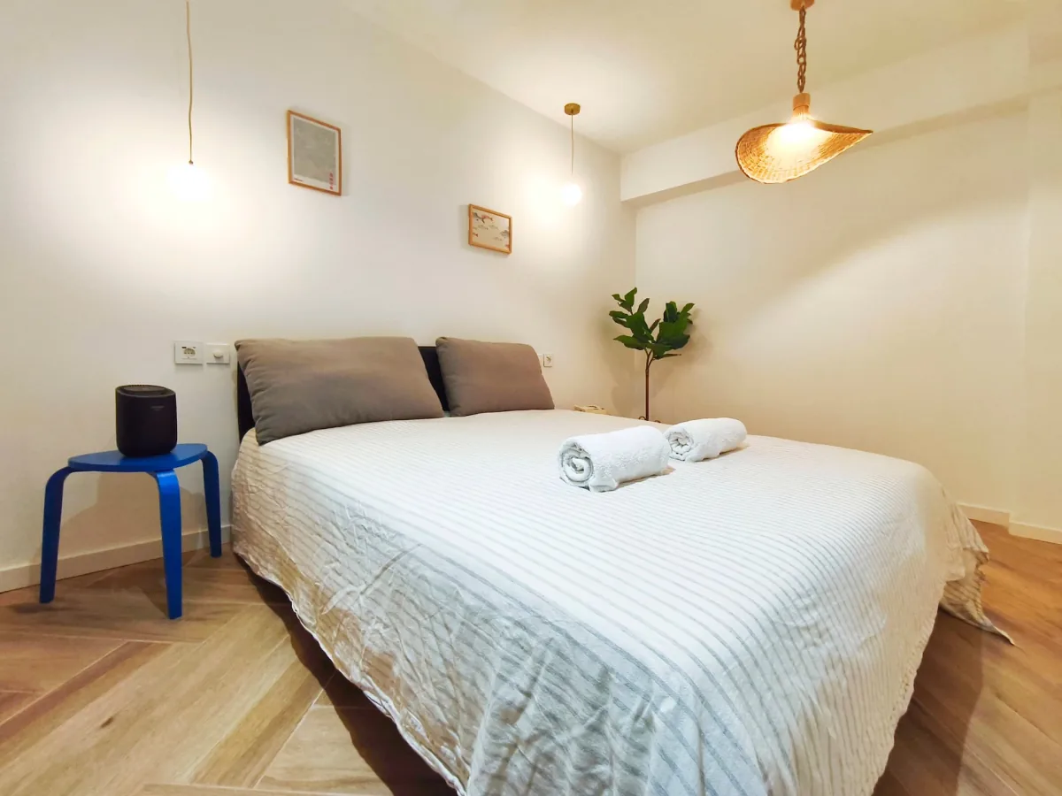 Dormitorio: cama con ropa blanca, cabecero bajo y estructura de madera clara contra la pared.